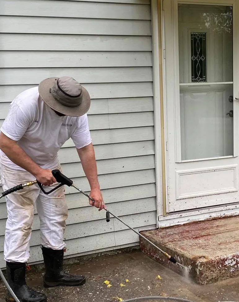 A professional at RyanPatrick Painting & Decorating carefully pressure-washing a concrete landing step to produce a beatiful, clean exterior.